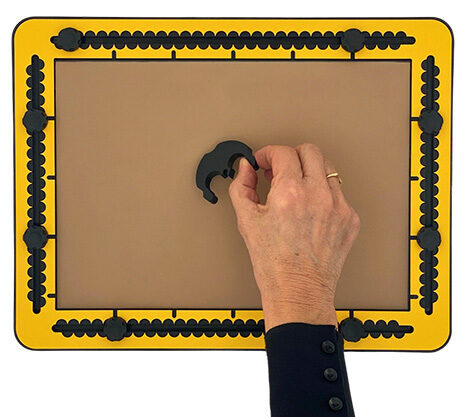 Two fingers lift the compass base from the TactiPad while holding one of the ears.