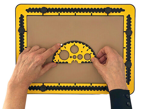 The protractor is on the drawing board. The thumb holds the bottom side. The pointing finger is measuring the 55 degrees corner. A pushpin is provided here.