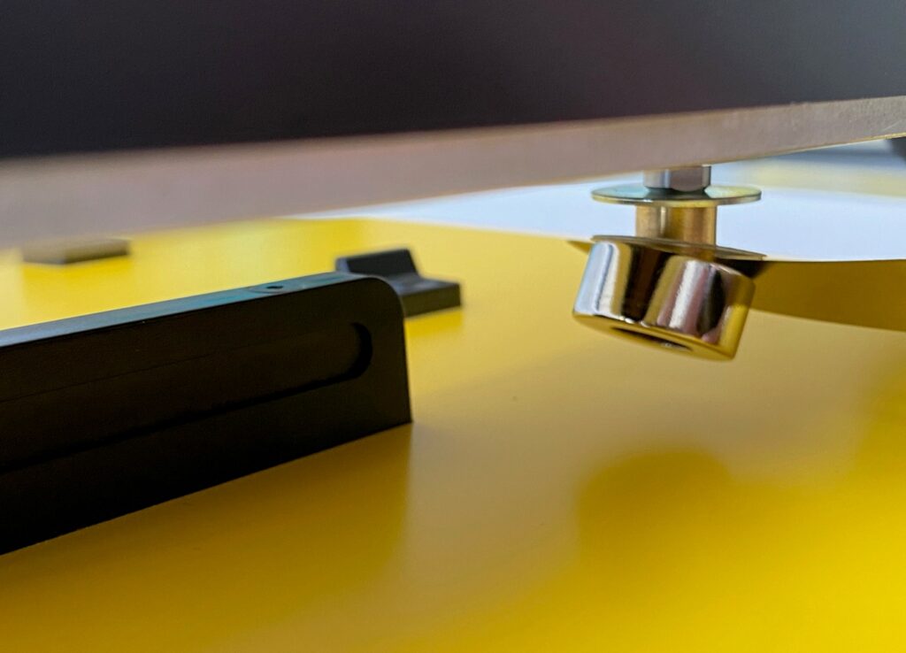 A blunt knife is inserted between the magnet and the shims / metal washer to remove the magnet from the assembly, allowing for the addition or removal of the shims